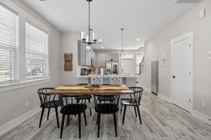A dining area with a wooden table and black chairs, a kitchen in the background, and a hallway leading to a door. - Creekside Bungalow-park Circle-15m Dtwn CHS (North Charleston)