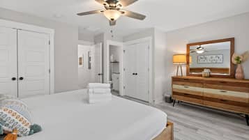 A bedroom with a large bed, a ceiling fan, white doors, a wooden dresser, and a mirror.