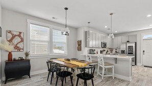 A modern kitchen with white cabinets, a central island, and a dining area with a wooden table and black chairs. - Creekside Bungalow-park Circle-15m Dtwn CHS (North Charleston)