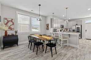Una cocina moderna con armarios blancos, una isla central y una zona de comedor con una mesa de madera y sillas negras.