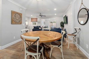 A dining area with a round wooden table and white chairs, a ceiling fan, and a large mirror on the wall. - Coastal Casa-old Village-5 Mins to Beach (Mount Pleasant)