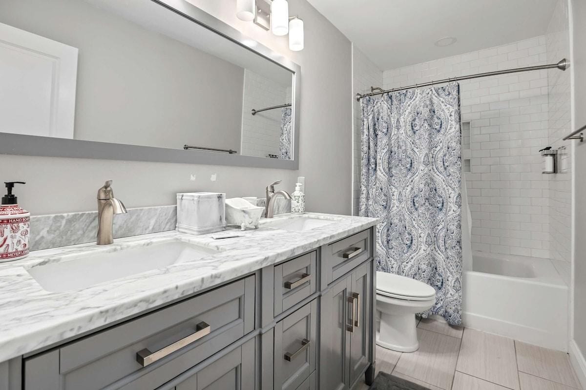 Une salle de bain avec un grand miroir, deux lavabos, des toilettes et un rideau de douche.