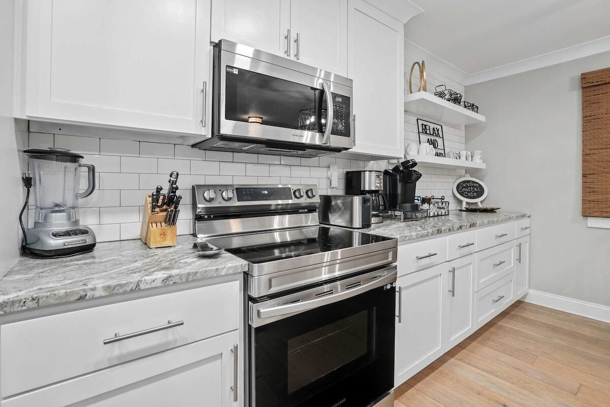 Et moderne køkken med hvide skabe, en rustfri stål mikroovn, en indbygget ovn og en kaffemaskine.