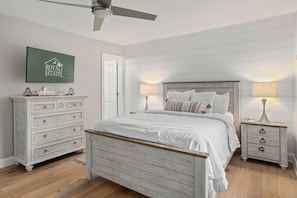 A bedroom with a bed, nightstands, a dresser, a ceiling fan, and a sign on the wall.