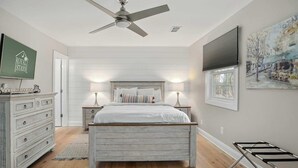 A bedroom with a bed, bedside tables, a ceiling fan, a dresser, a window with blinds, and a painting on the wall. - Coastal Casa-old Village-5 Mins to Beach (Mount Pleasant)