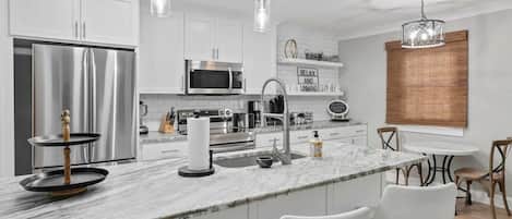 A modern kitchen with white cabinets, stainless steel appliances, and a marble island.