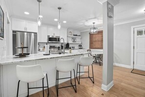 Cozinha moderna com armários brancos, eletrodomésticos de aço inoxidável e uma ilha de mármore com banquetas.