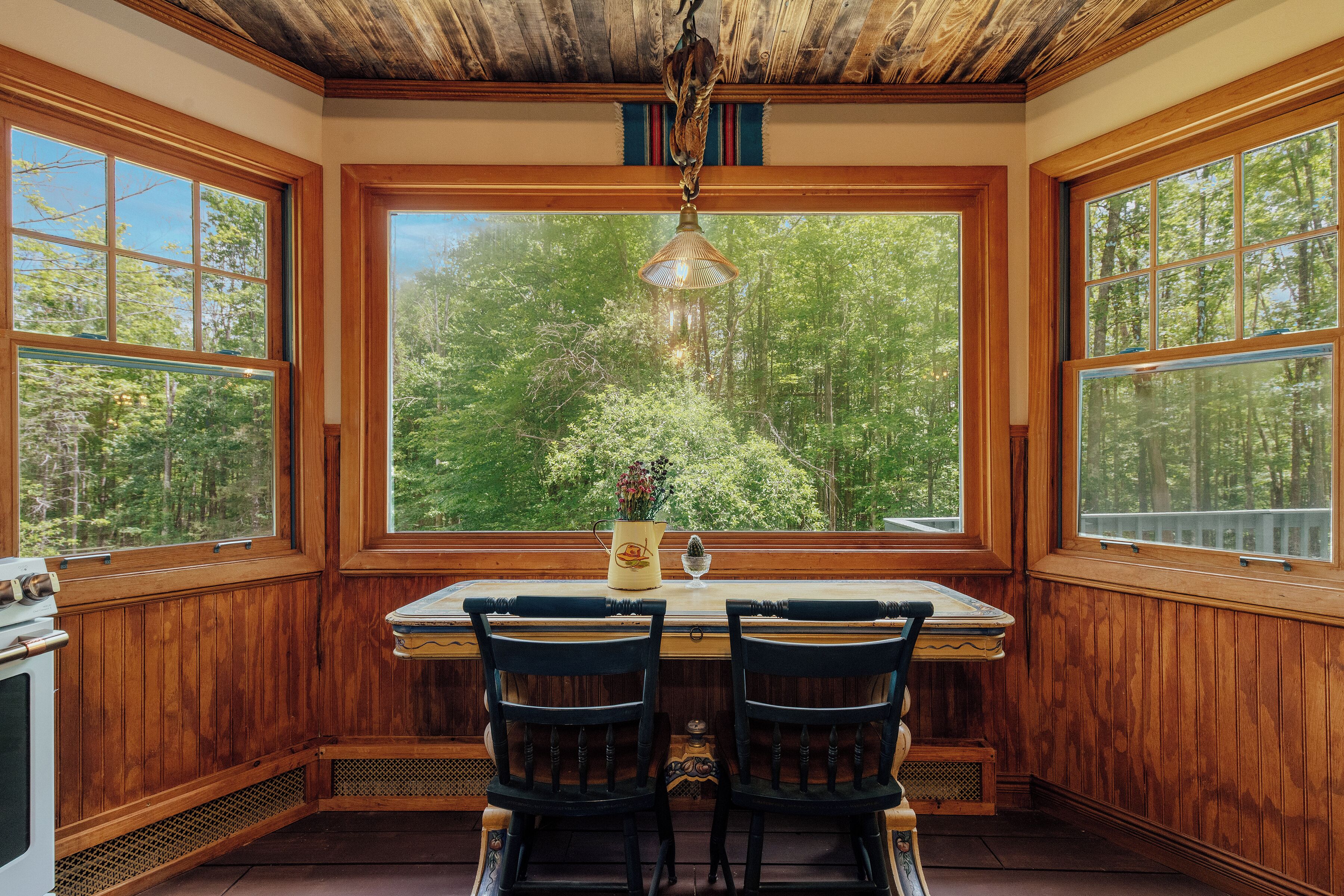 A wooden interior with a large window, a table, two chairs, and a hanging light fixture.