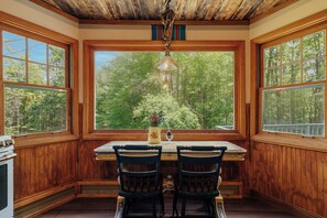 A wooden interior with a large window, a table, two chairs, and a hanging light fixture.