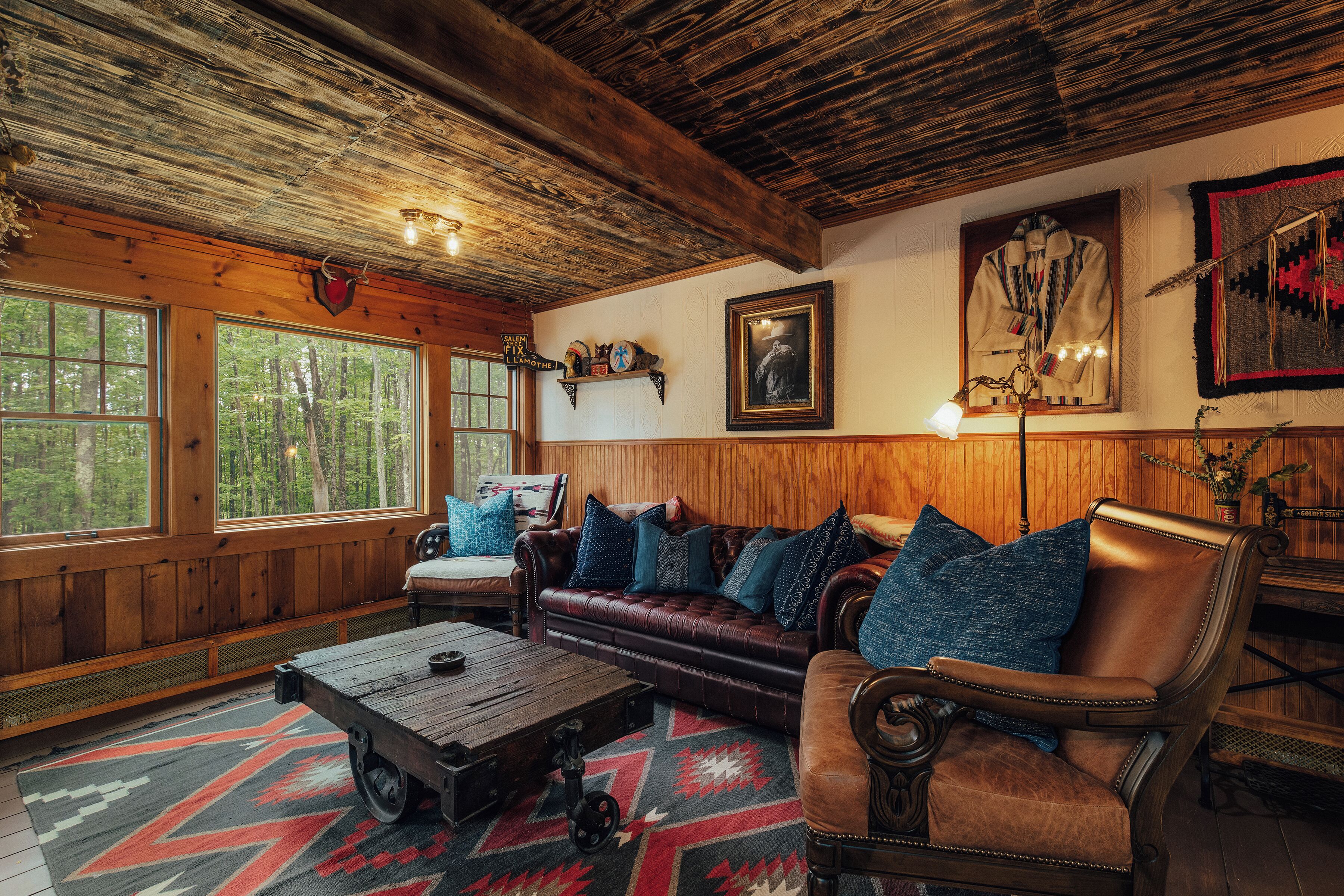 A cozy cabin interior with a leather sofa, a wooden coffee table, and a large window offering a view of the forest.