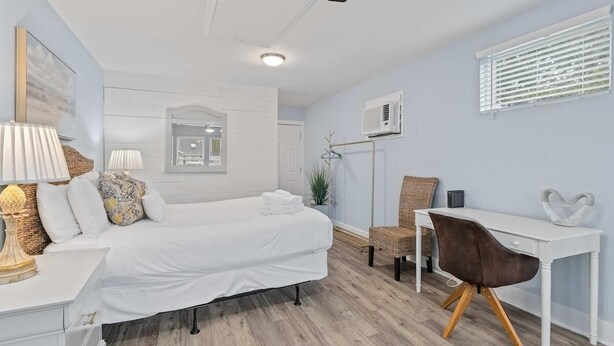 A modern bedroom with a bed, bedside table, chair, desk, and a window with blinds. - The Costal Haven - 5 Min Beach, 15 Min to DT (Mount Pleasant)