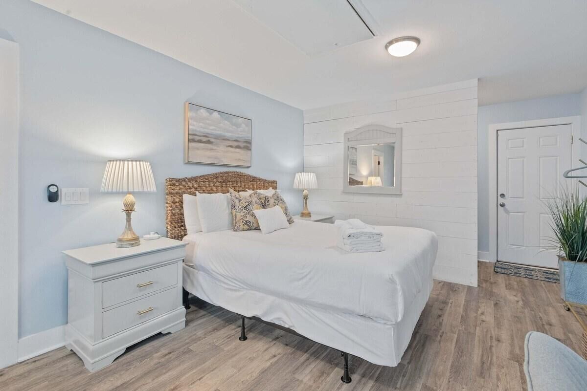 Un dormitorio con cama, mesitas de noche, un espejo y una puerta.