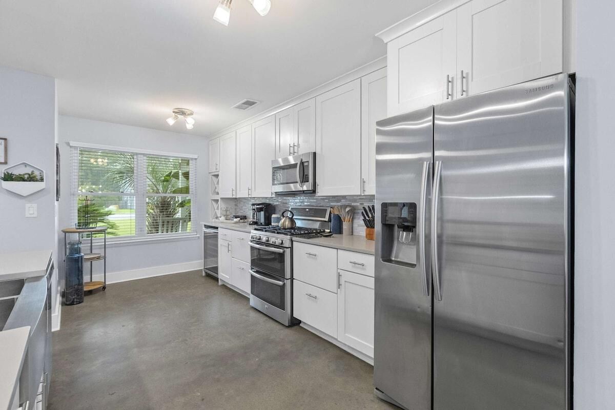 A modern kitchen with stainless steel appliances, white cabinets, and a large window with a view of greenery.