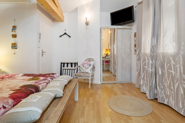 A bedroom with a bed, a chair, a TV, and a door leading to another room.