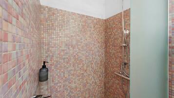 Zona de ducha con pared de azulejos, cabezal de ducha de mano y una botella de champú.