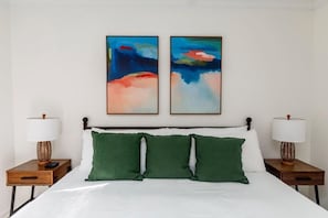 A hotel room with a large bed, two nightstands, and two abstract paintings on the wall. - Southern Serenity, Fenced in Yard, Pet Friendly (Mount Pleasant)