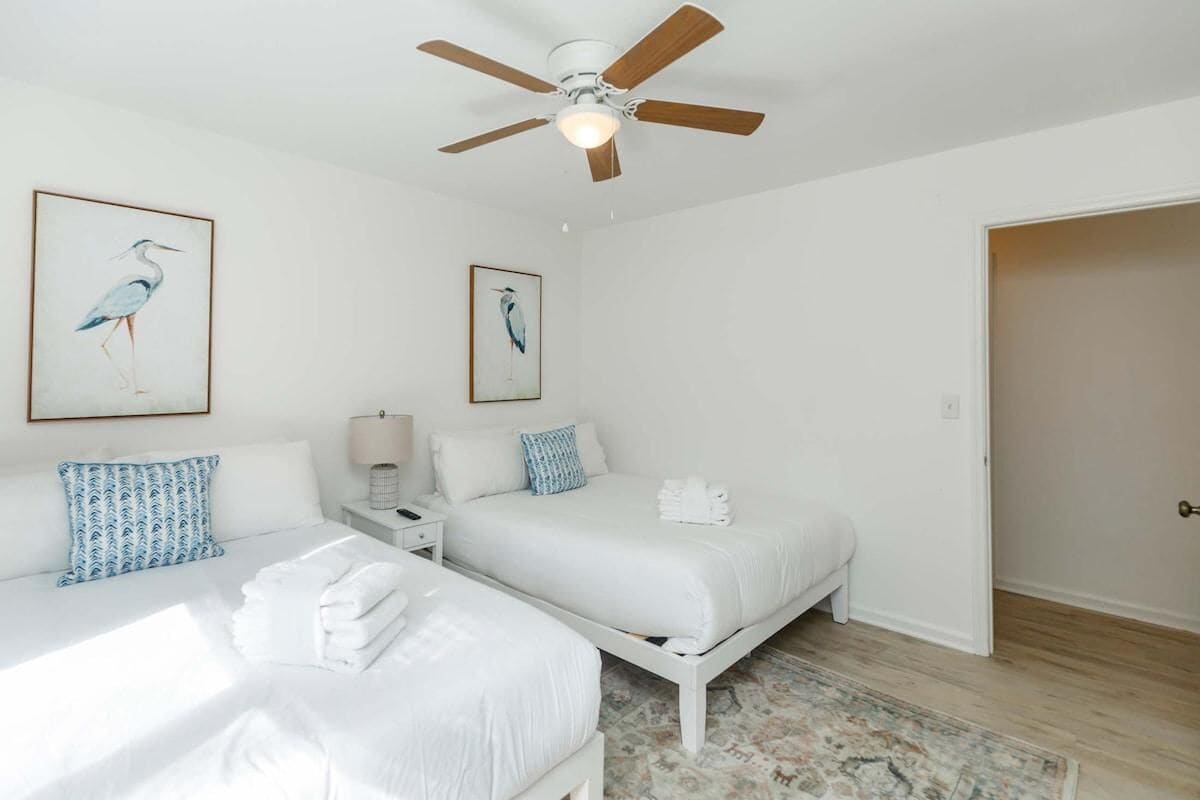 A hotel room with two beds, a ceiling fan, and artwork of birds on the walls.