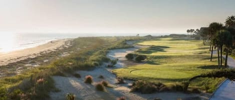 Un parcours de golf avec un sentier sablonneux, de l’herbe verte et des palmiers.