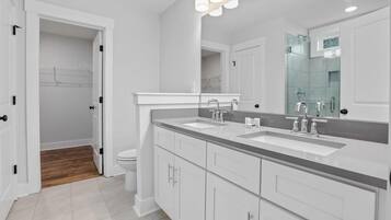 A modern bathroom with a double sink vanity, a large mirror, and a walk-in closet.