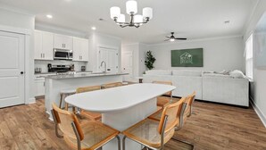 Una cocina moderna con armarios blancos, una isla central con asientos, una lámpara de araña y un ventilador de techo.