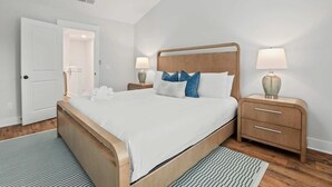 Un dormitorio moderno con una cama de madera, dos mesitas de noche con lámparas, una puerta que da a un baño y un tapete a rayas.
