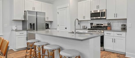 Una cocina moderna con armarios blancos, electrodomésticos de acero inoxidable y una isla central con taburetes de bar.