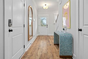 Un pasillo con puertas blancas, suelo de madera, un espejo y una encimera con estampado.