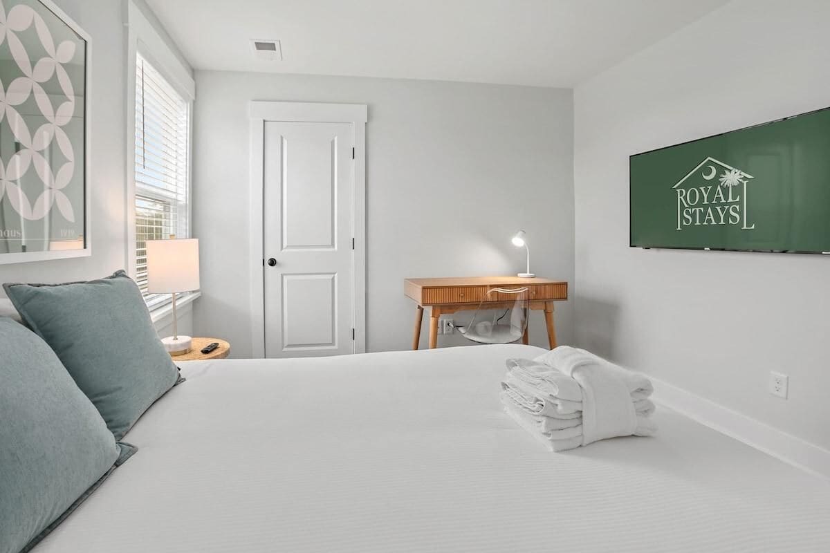 Een hotelkamer met een bed, nachtkastje, lamp, opgevouwen handdoek, deur en een bordje aan de muur.