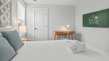 Een hotelkamer met een bed, nachtkastje, lamp, opgevouwen handdoek, deur en een bordje aan de muur.