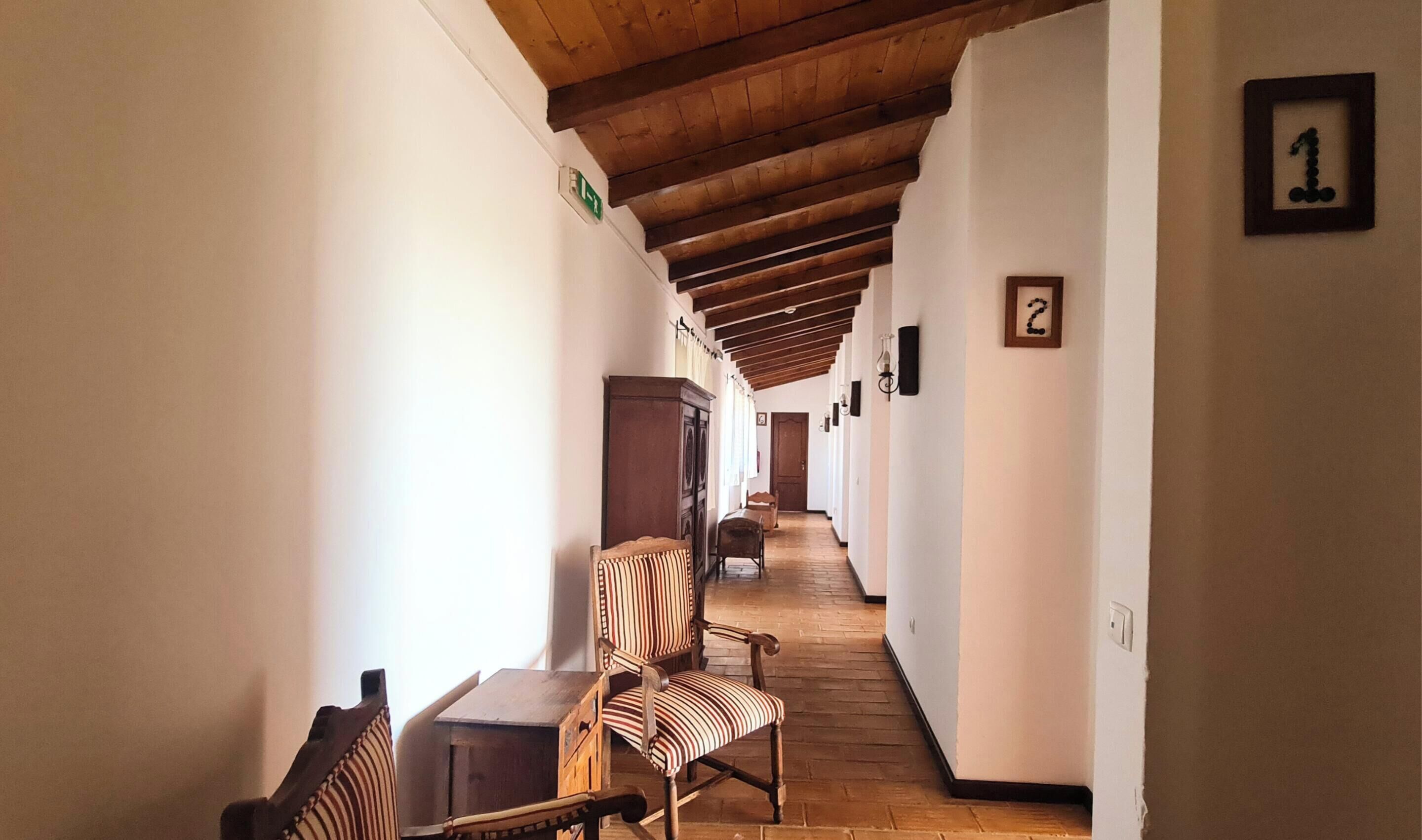 A hallway with wooden beams, numbered rooms, and striped chairs.