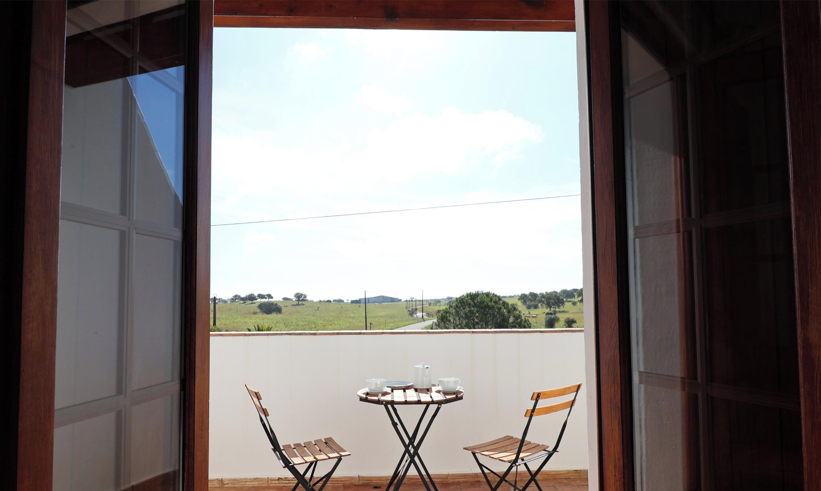A balcony with a table and two chairs, overlooking a grassy landscape.