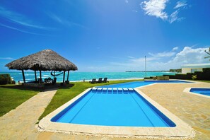 Ein Poolbereich mit einem Reetdach, Liegestühlen und Blick aufs Meer.