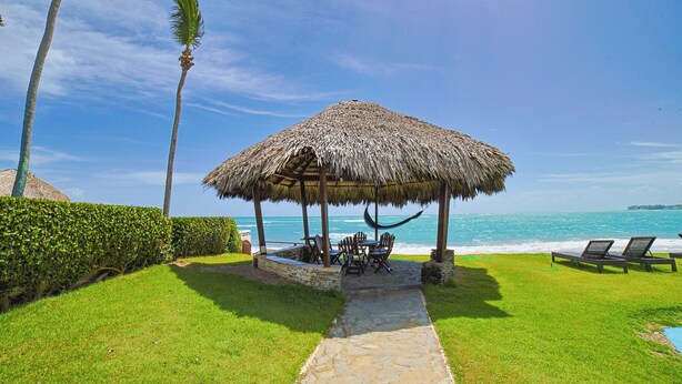 A thatched-roof pavilion with outdoor seating, a stone pathway, and a view of the ocean. - Bright & Moderm 2BR/Aparment Comfort & Style  (Cabarete)