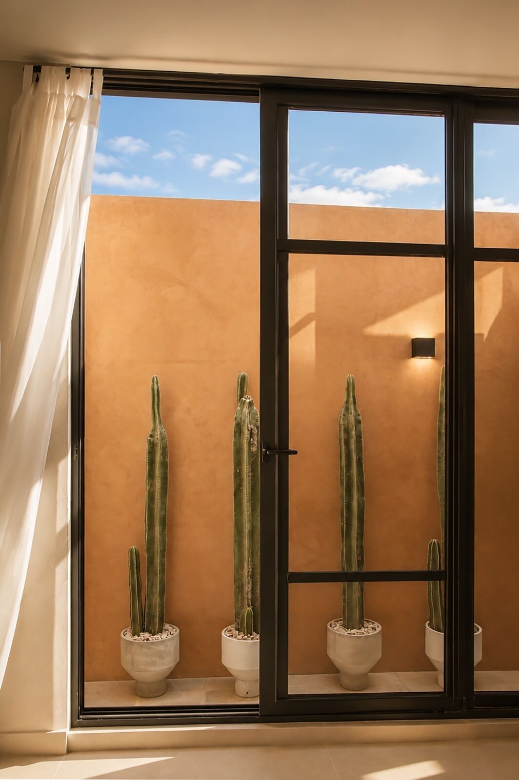 A room with a sliding glass door, a view of the sky, and three potted cacti.
