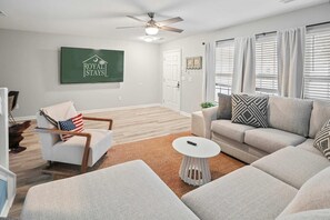 A modern living room with a ceiling fan, a flat-screen TV, a sofa, a chair, and a coffee table. - Chucktown Charm- 8 Mins to Credit One (Charleston)