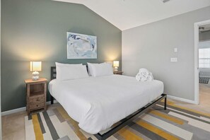 Un dormitorio moderno con una cama grande, dos mesitas de noche con lámparas, un cuadro en la pared y vistas a un balcón.