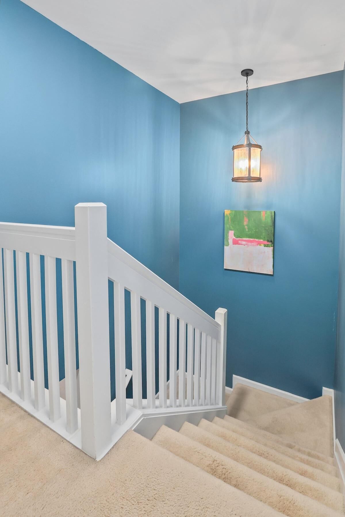 A staircase with white railings leading to a landing with a blue wall and a hanging light fixture.