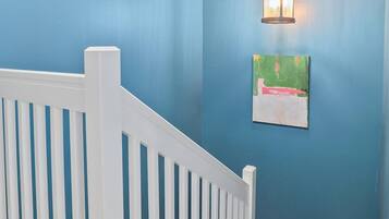 A staircase with white railings leading to a landing with a blue wall and a hanging light fixture.