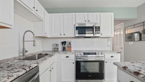 A modern kitchen with white cabinets, a stainless steel oven, a microwave, and a granite countertop. - Chucktown Charm- 8 Mins to Credit One (Charleston)