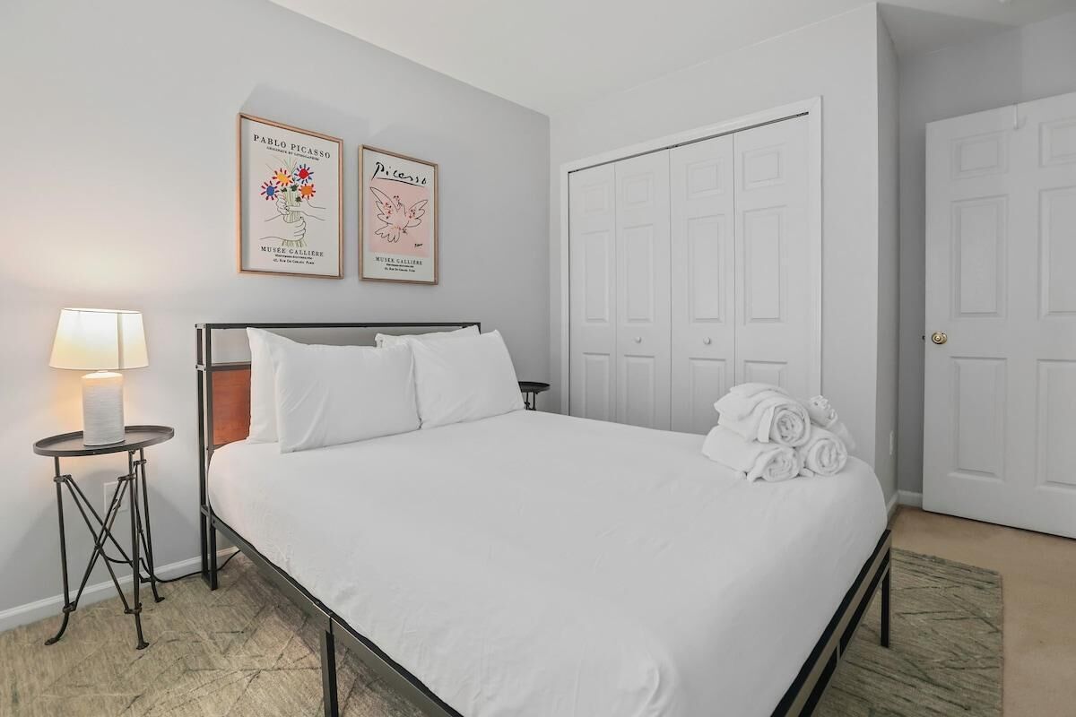A neatly made bed with white linens, a bedside lamp, and two framed artworks on the wall.
