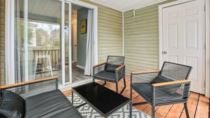 A covered patio with two black wicker chairs and a black table, a sliding glass door, and a white door. - Chucktown Charm- 8 Mins to Credit One (Charleston)