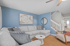 A living room with a light grey sectional sofa, a small white coffee table, and a white armchair with an American flag pillow. There is a framed abstract painting on the wall and a decorative mirror above the sofa. - Chucktown Charm- 8 Mins to Credit One (Charleston)