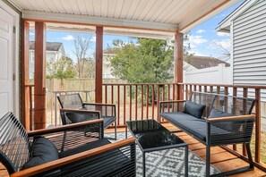 A covered patio with wooden flooring, black and wooden furniture, and a view of a residential neighborhood. - Chucktown Charm- 8 Mins to Credit One (Charleston)