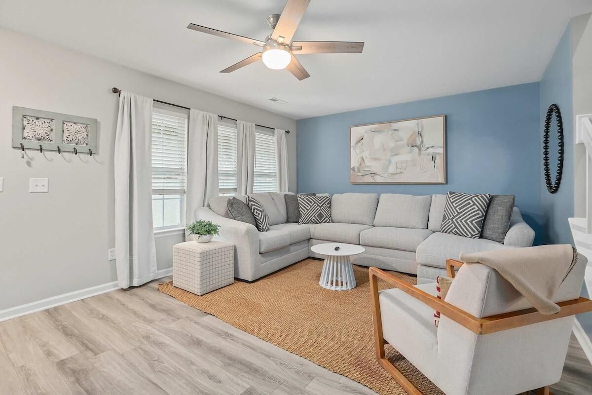 A living room with a light gray sectional sofa, a white coffee table, a small side table, and a ceiling fan.