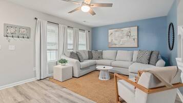 A living room with a light gray sectional sofa, a white coffee table, a small side table, and a ceiling fan.