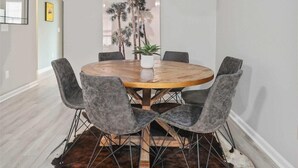 A dining area with a round wooden table, six grey upholstered chairs, a hanging light fixture, and a cowhide rug. - Chucktown Charm- 8 Mins to Credit One (Charleston)