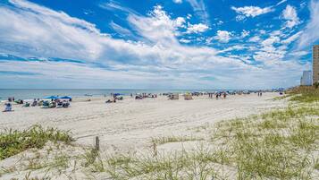 A beach with sand, grass, and a clear sky.