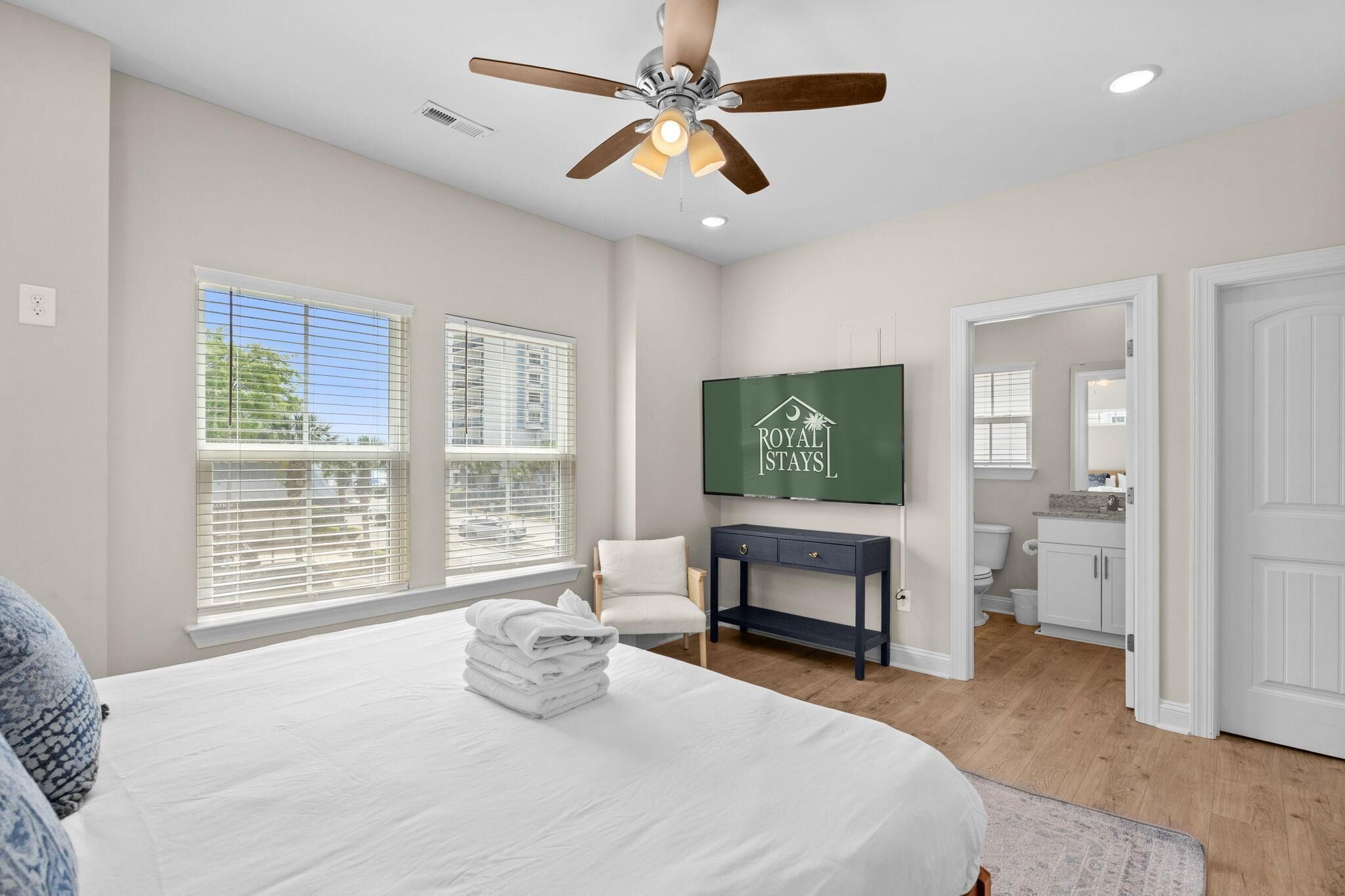 A bedroom with a bed, a ceiling fan, a TV on the wall, and a view of the bathroom.