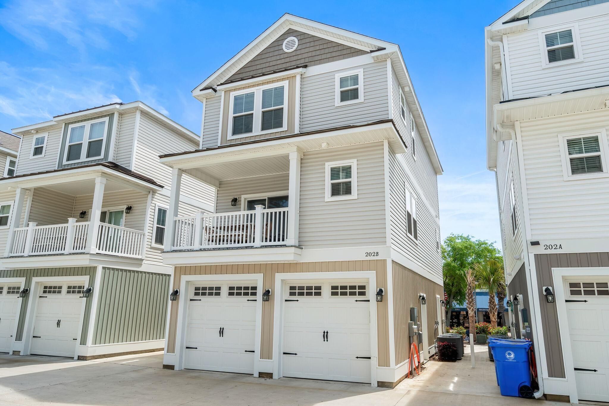 A multi-story residential building with a balcony, garage doors, and a clear sky.