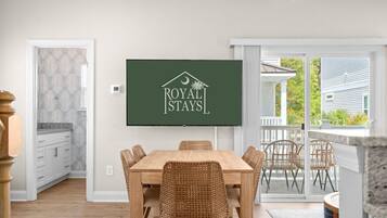 A dining area with a table and chairs, a television displaying 'ROYAL STAYS' logo, and a view of the outside.